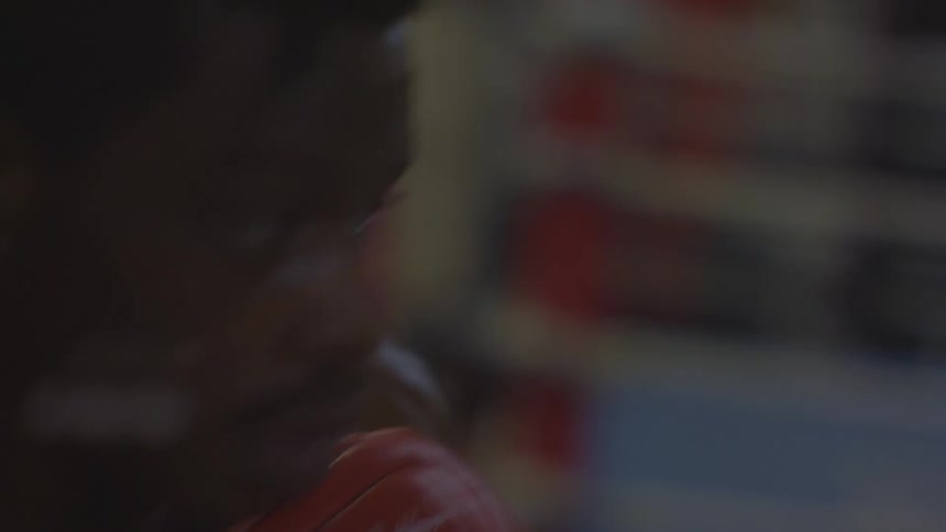 A determined male boxer in slow motion relentlessly punches a heavy bag in a dimly lit gym