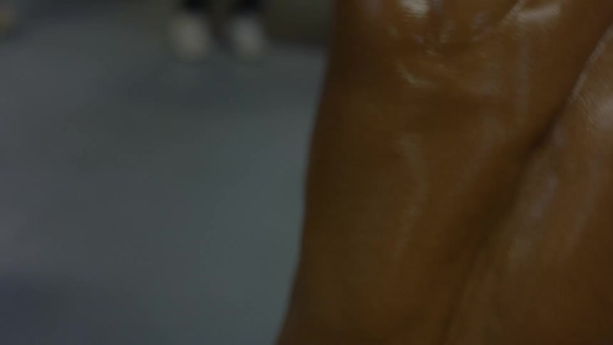 A close up shot of a muscular and athletic man's glistening back as he dances energetically in a dimly lit room