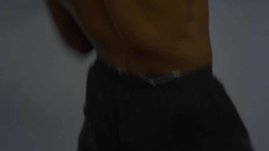A close-up shot of a muscular, sweaty man's back as he performs an energetic dance, showcasing his defined muscles