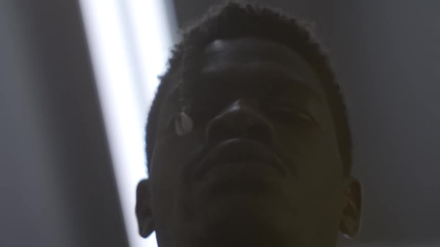 A moody low-angle close-up of a young Black man's face in silhouette as he closes his eyes in quiet contemplation