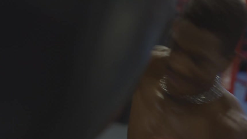 Close-up slow motion shot of a muscular boxer hitting a punching bag until exhaustion in a dark gym