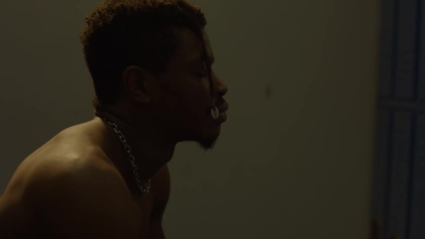 A focused Black man sits in a dimly lit locker room, mentally preparing for a challenge