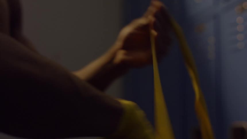 A boxer carefully wraps his hands with yellow athletic tape in a dark locker room
