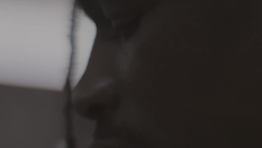 An artistic close-up of a thoughtful Black person's face in profile, shot in slow motion in a dimly lit room
