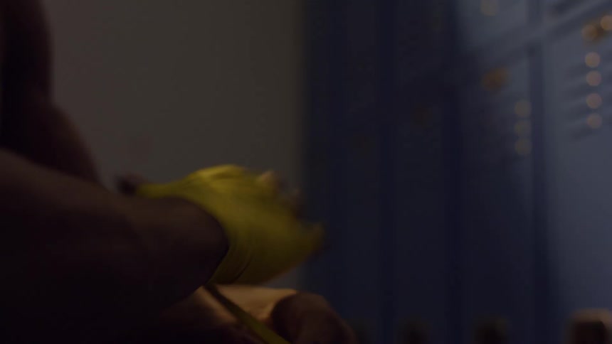 Close up of a fighter meticulously wrapping their hands with yellow tape in a dimly lit locker room