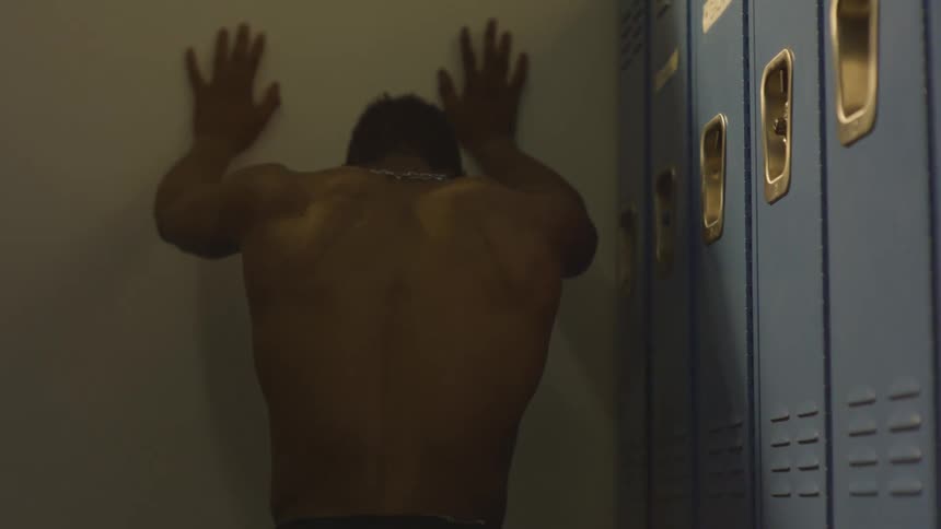 A distraught and muscular athlete expresses his frustration alone in a dimly lit locker room