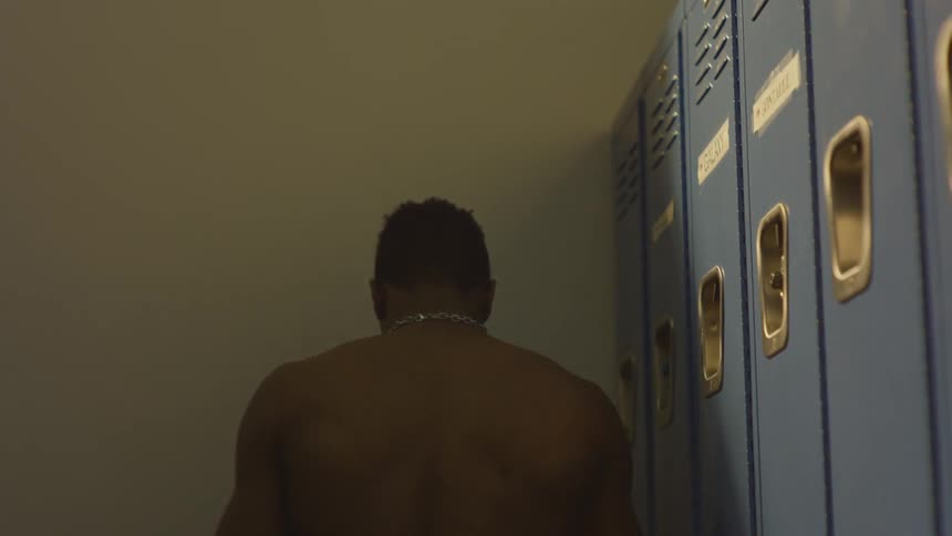 A muscular athlete mentally prepares himself in a dimly lit locker room before a competition