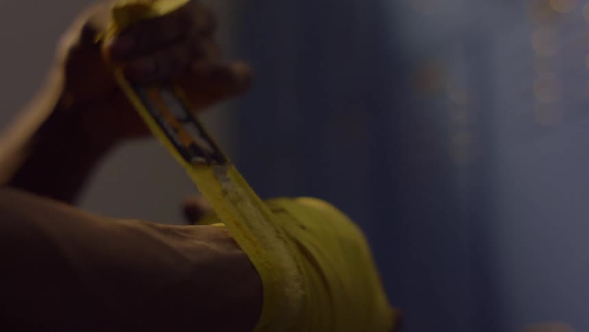 A close-up of a fighter wrapping their hands with yellow tape in slow motion before training