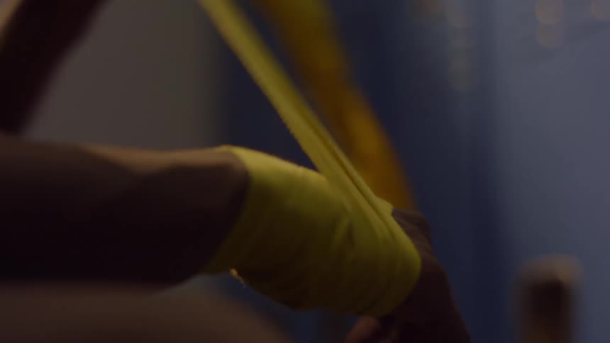 A fighter meticulously wraps their hands with yellow tape in a dimly lit locker room before a match