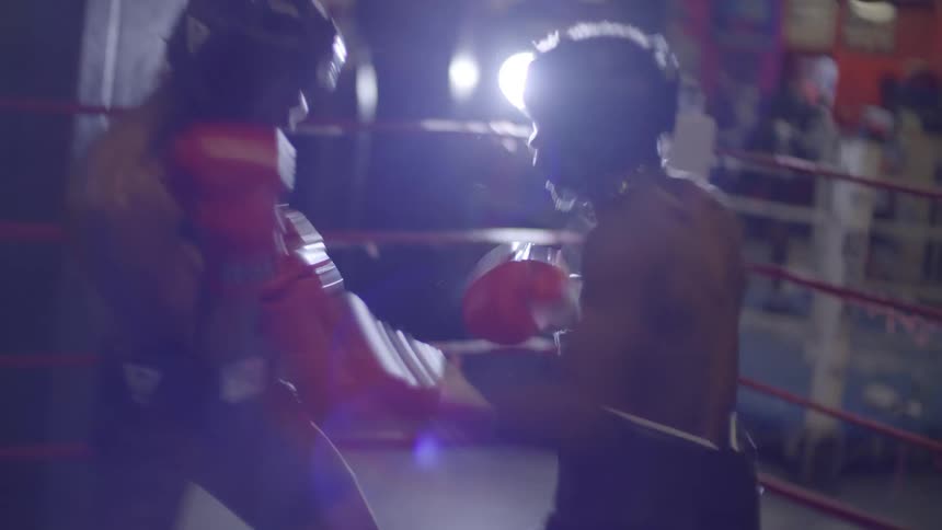 Two muscular boxers spar intensely in a dramatically backlit ring, exchanging fast and powerful punches