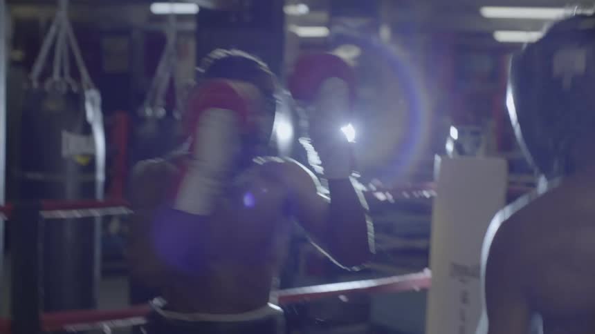 Two muscular boxers in headgear trade powerful punches in slow motion during an intense sparring session inside a gym's boxing ring