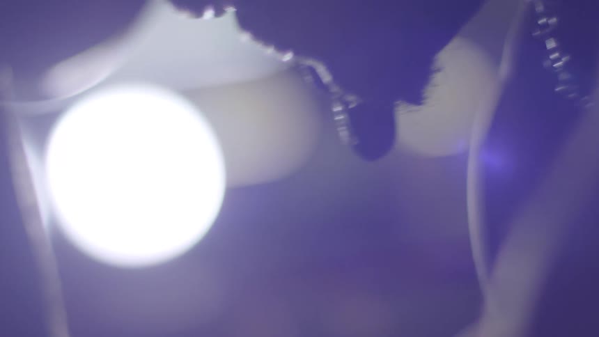 A stylized macro shot of a dark, viscous liquid slowly dripping in silhouette against a bright light source