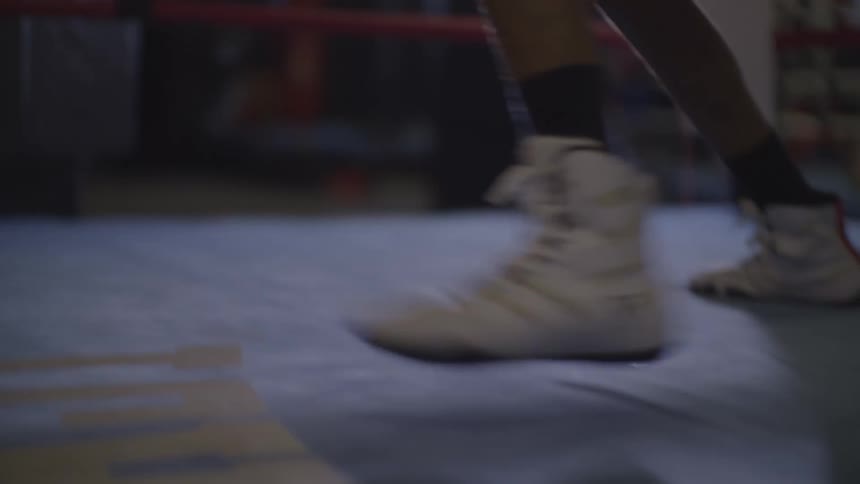 Dynamic low-angle shot of two boxers' feet shuffling across the canvas of a dimly lit boxing ring