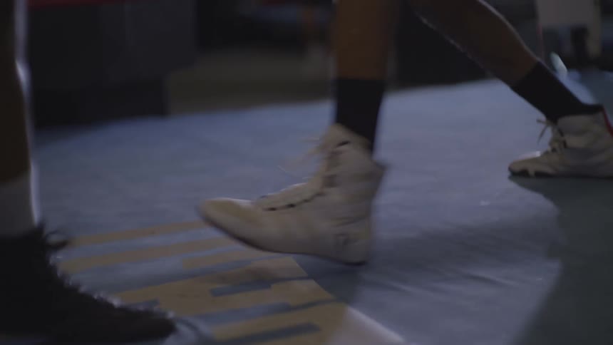 A dramatic slow-motion close-up captures the intricate footwork of two boxers sparring in the ring