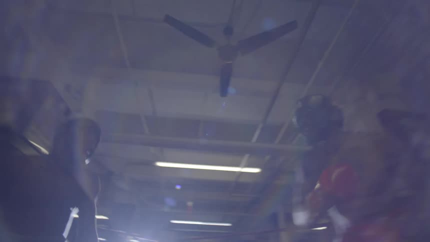 Low-angle shot of two boxers sparring intensely in a dimly lit boxing ring