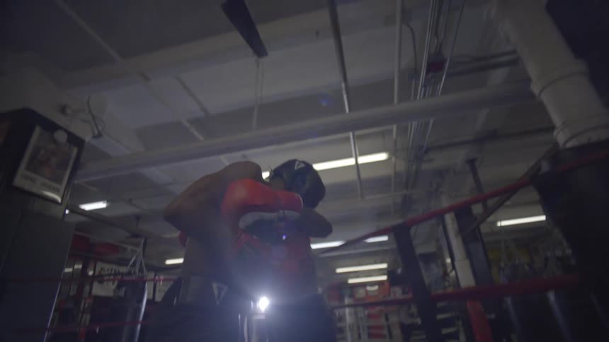 Low angle slow motion shot of two boxers sparring intensely in a dimly lit boxing ring