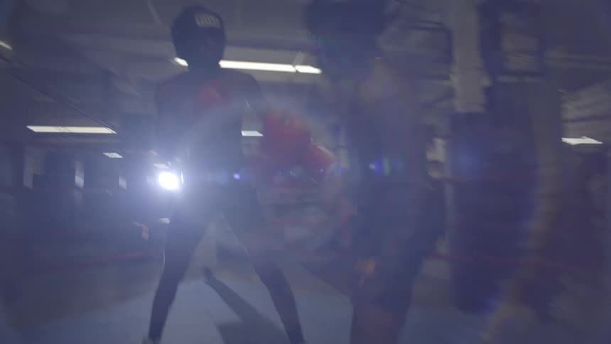Two determined male boxers spar in slow motion inside a dimly lit boxing ring at a gym
