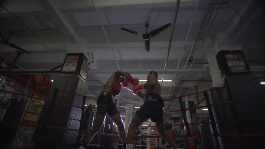 Two boxers trade punches in slow motion during an intense sparring session inside a dramatically lit boxing ring