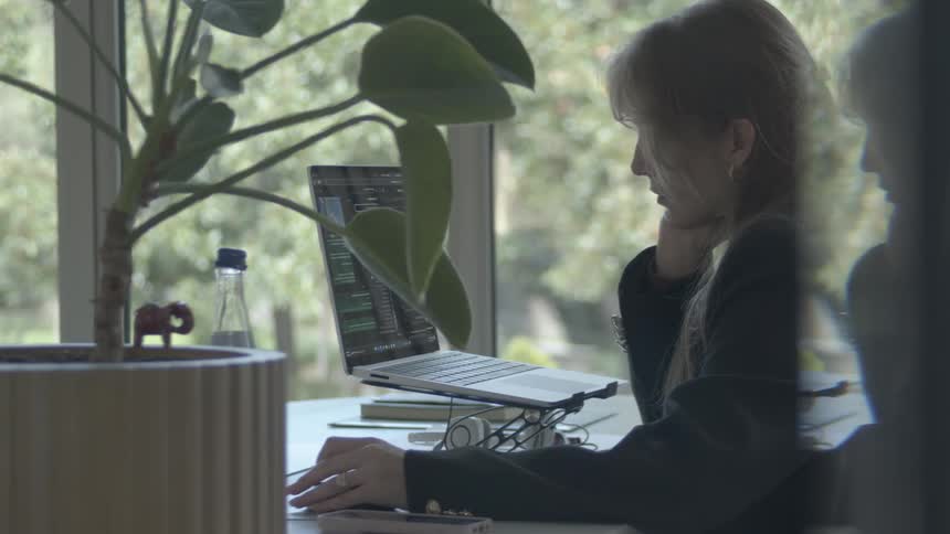 Side profile shot of a focused woman working on her laptop at a desk in a bright, modern workspace