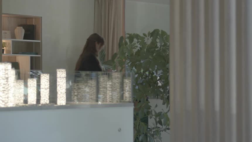 A woman sits down to work at her desk in a modern, stylish office with minimalist decor and indoor plants