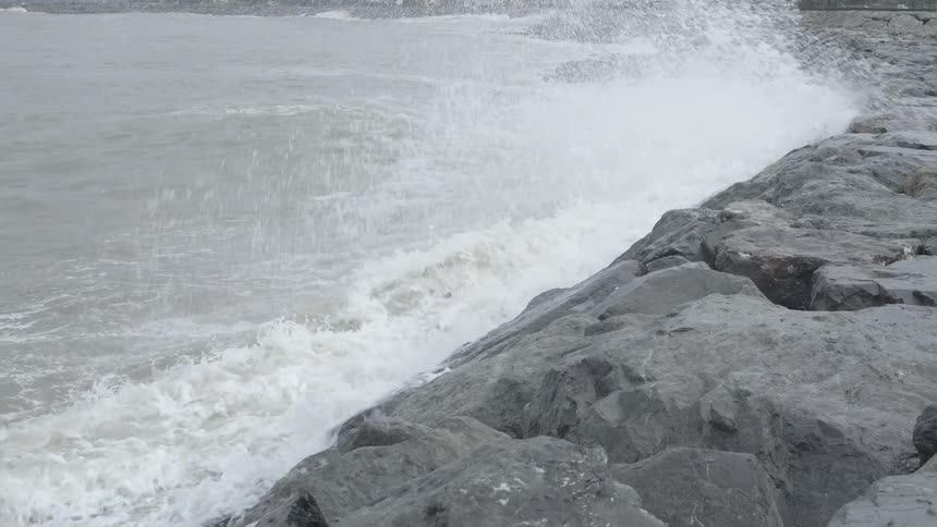 Powerful ocean waves crash against a rocky breakwater in dramatic slow motion on an overcast day