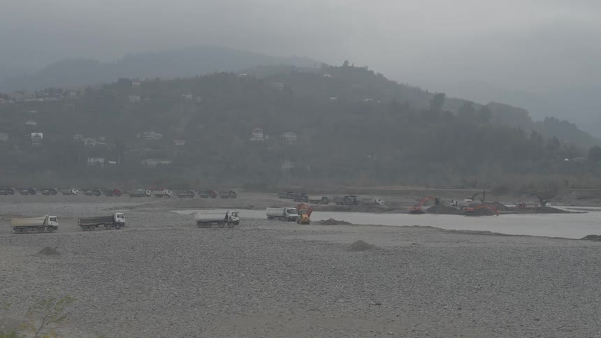 Excavators and dump trucks work at a riverbed quarry mining for gravel on a foggy day