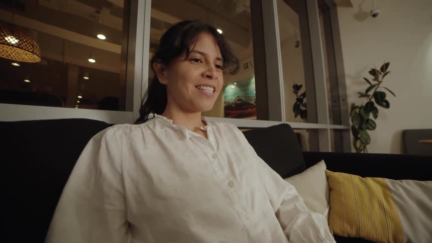 A happy woman finishes working on her laptop and smiles contentedly while relaxing on a comfortable sofa in a modern space at night