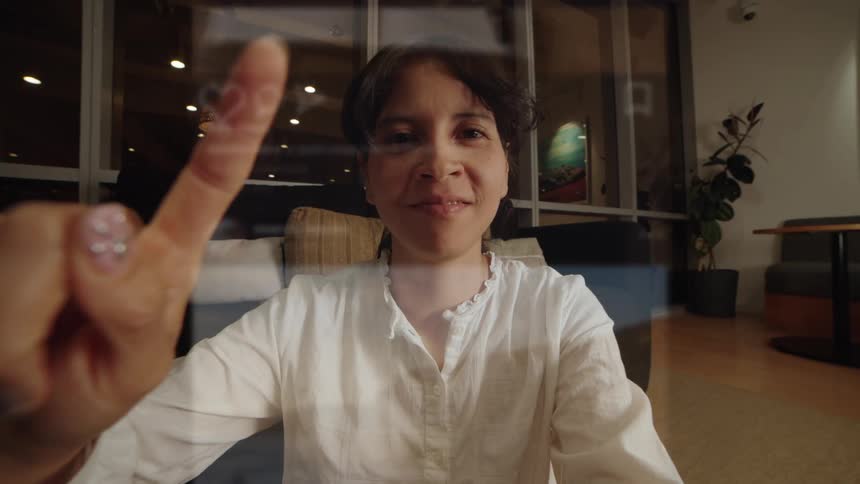 POV shot of a woman happily engaging with social media on a futuristic transparent display, scrolling through content and reacting with animated likes