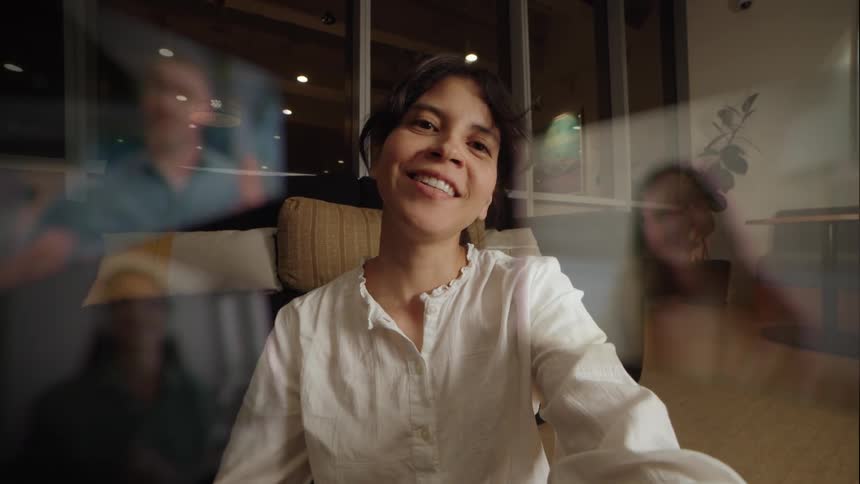 A smiling woman enjoys a virtual meeting, waving enthusiastically at her friends and family on the screen