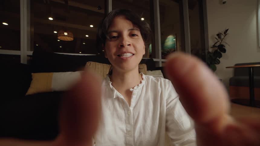 First-person perspective of a woman smiling and talking on a video call at night in a modern living room