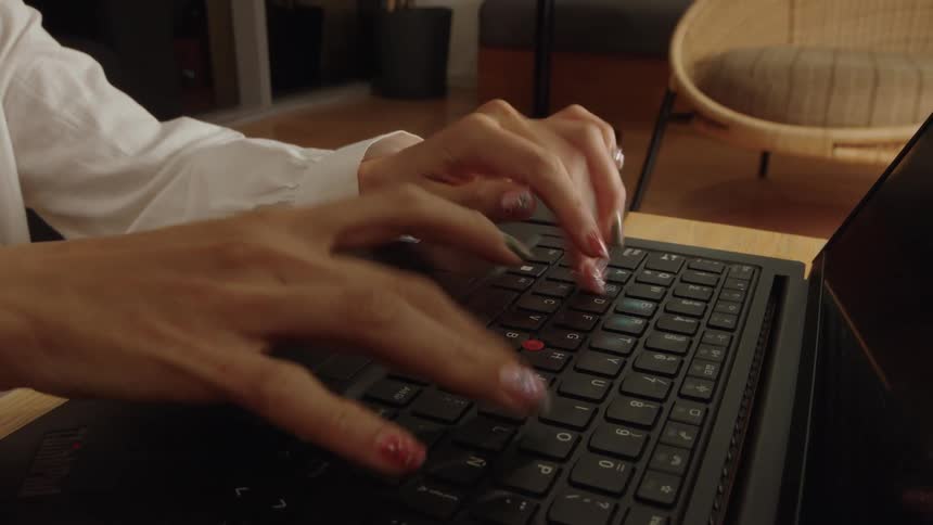 A close-up shot of a woman's manicured hands typing on a laptop keyboard at her desk
