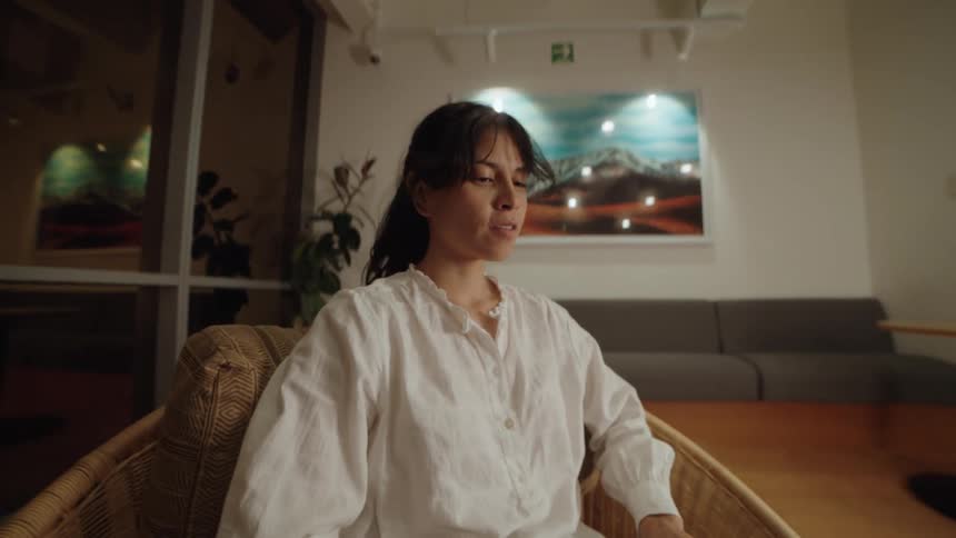 A woman smiles as she types on her laptop in a cozy, modern lounge at night, captured in a slow-motion shot