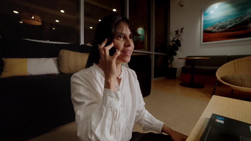 A woman reacts with excitement and surprise to good news during a phone call while working late at night