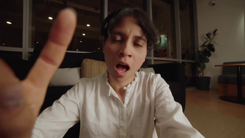 A woman's expressive face shows shock and then delight while talking on a video call, with her hand near the camera
