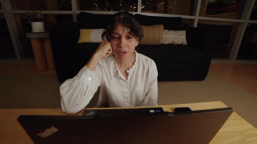 A woman's expression changes from surprise to happiness while on a video call at night in her modern apartment