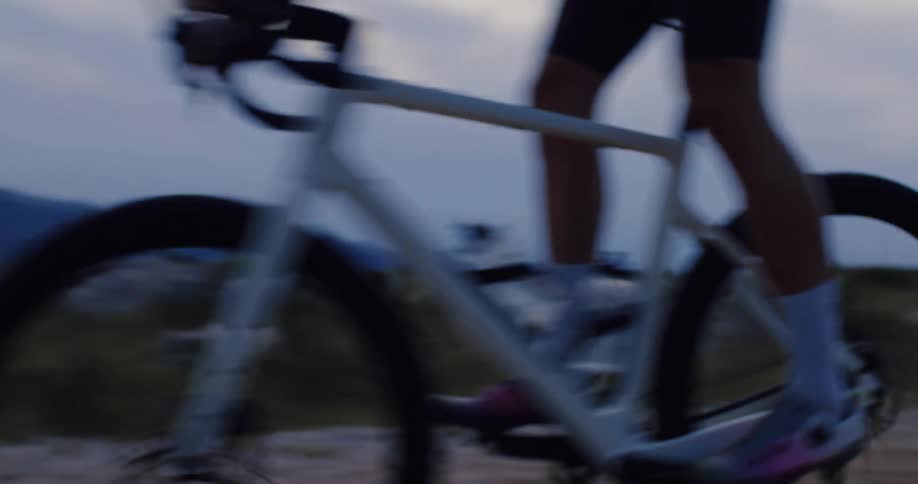 A male cyclist enjoys an evening ride on his gravel bike along a scenic dirt path next to the water