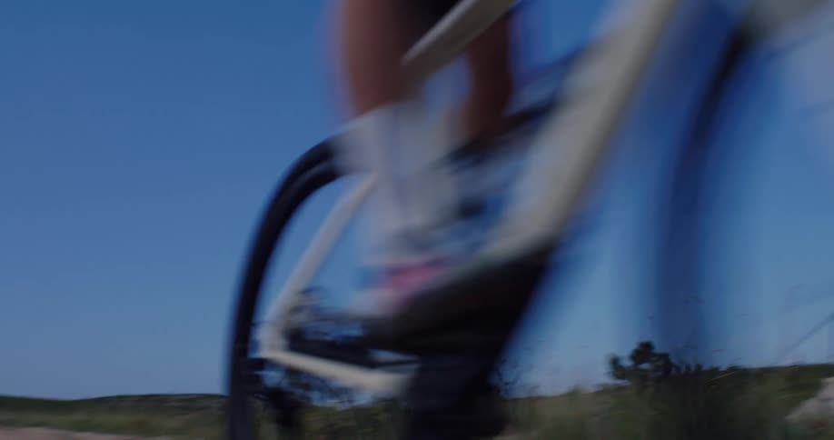 A man rides a bicycle at speed down a gravel road creating motion blur with mountains in the background