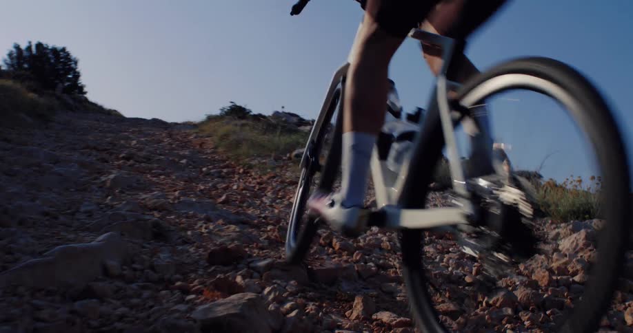 Low angle slow motion shot of a cyclist pedaling up a steep and rocky off-road trail