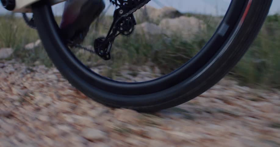 Slow-motion close-up of a bicycle's rear wheel, gear, and chain spinning while riding on a gravel trail