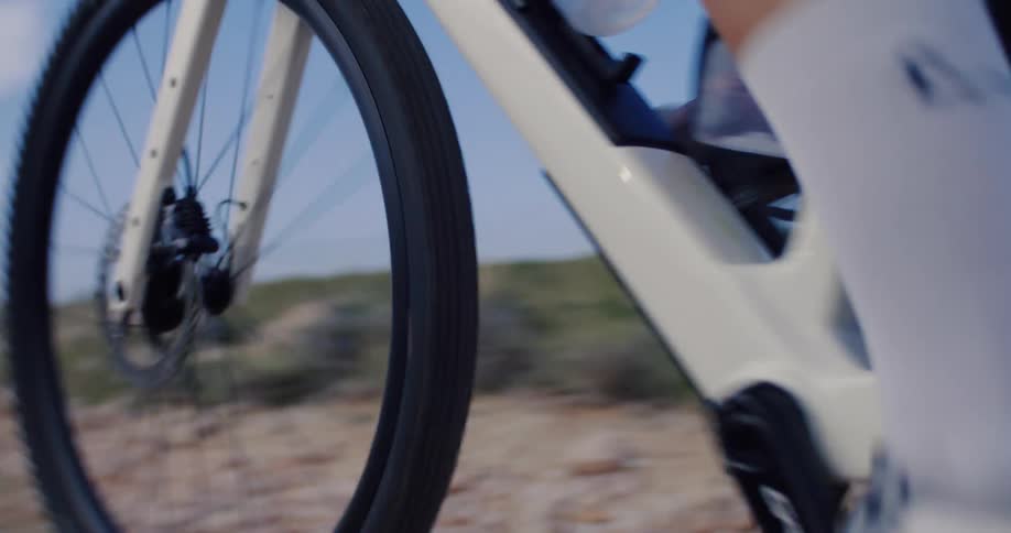 Cinematic close-up of a cyclist pedaling a gravel bike on a rugged dirt trail in slow motion