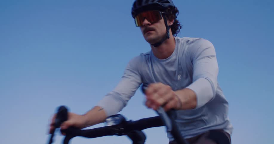 Slow motion shot of a male cyclist riding his gravel bike up a coastal path with the ocean in the background