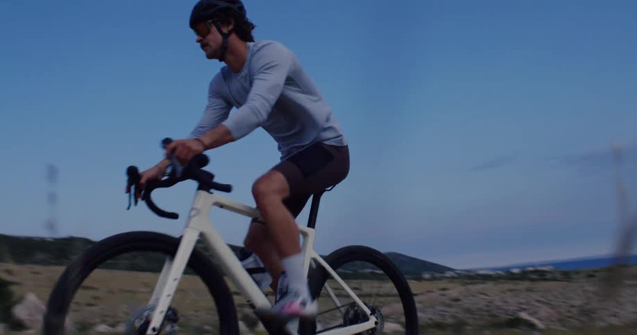 A male cyclist rides his gravel bike along a rugged coastal path in a cinematic slow-motion shot