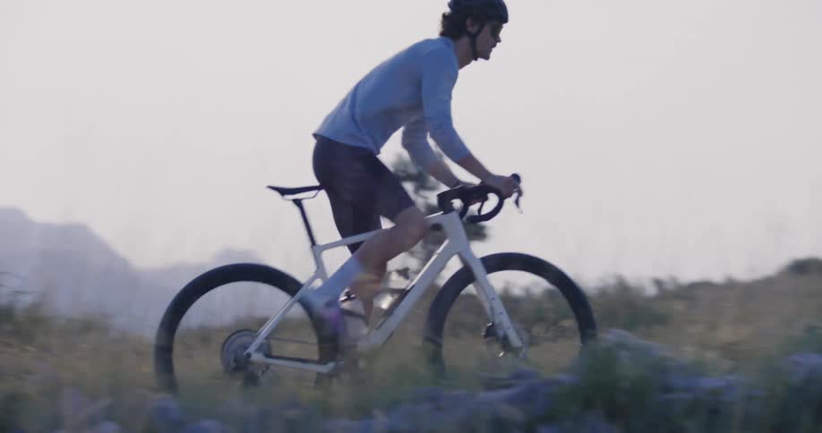 A lone cyclist navigates a rugged coastal trail during a challenging dusk ride through the mountains