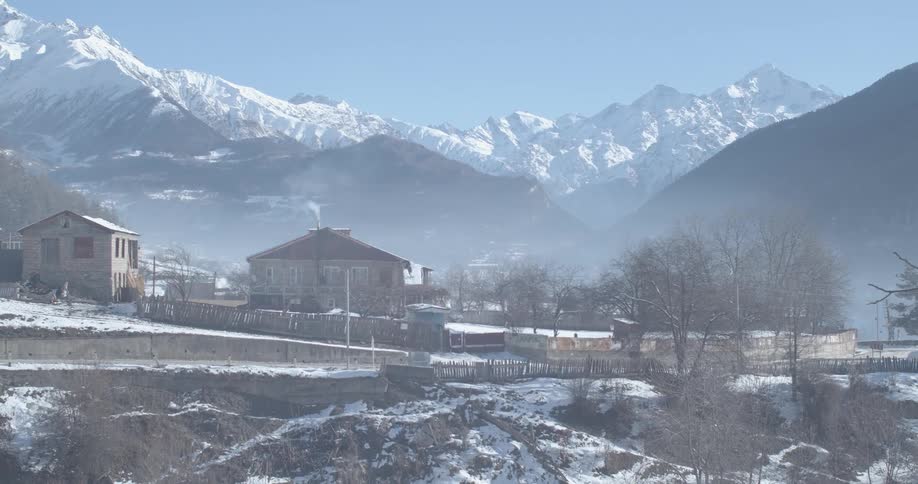 A tranquil mountain village is shrouded in morning mist as the sun shines on the snowy peaks above