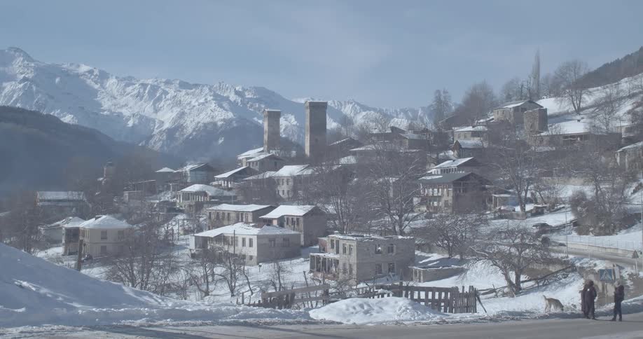 A wide scenic shot of the historic village of Mestia, Georgia, with its iconic Svaneti towers, nestled in a snow-covered mountain valley during winter