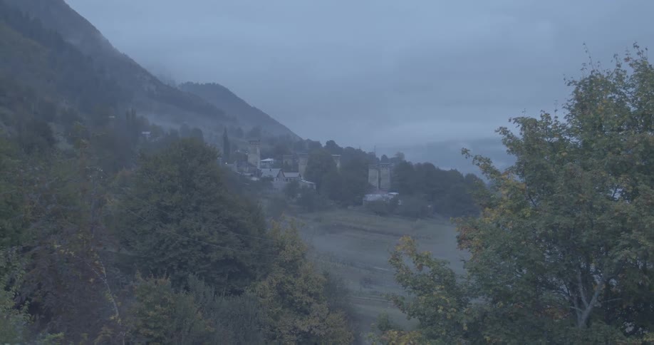 A mysterious mountain village with Svaneti towers is shrouded in fog on a gloomy, overcast day