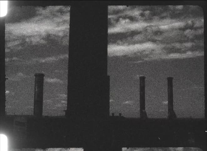 Silhouetted view of industrial factory smokestacks from a moving elevated train in grainy black and white