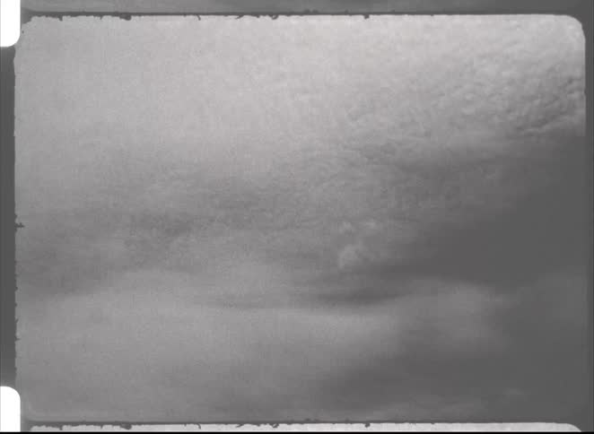 Vintage, grainy black and white footage shows a time-lapse of clouds moving across the sky