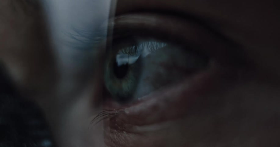 An extreme close-up macro shot of a person's green eye focusing and blinking in a dark room