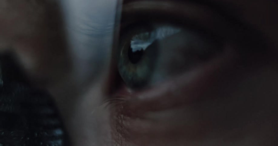 An intense macro shot of a person's eye, showing the reflection of a bright screen in their pupil as they focus intently in the dark